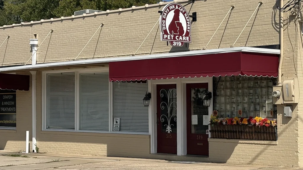 Storefront of Dog Days Inn & Cat Nappery Pet Care at 319 Williams Street in Fayetteville, NC, with a maroon awning and hanging dog-and-cat logo sign.